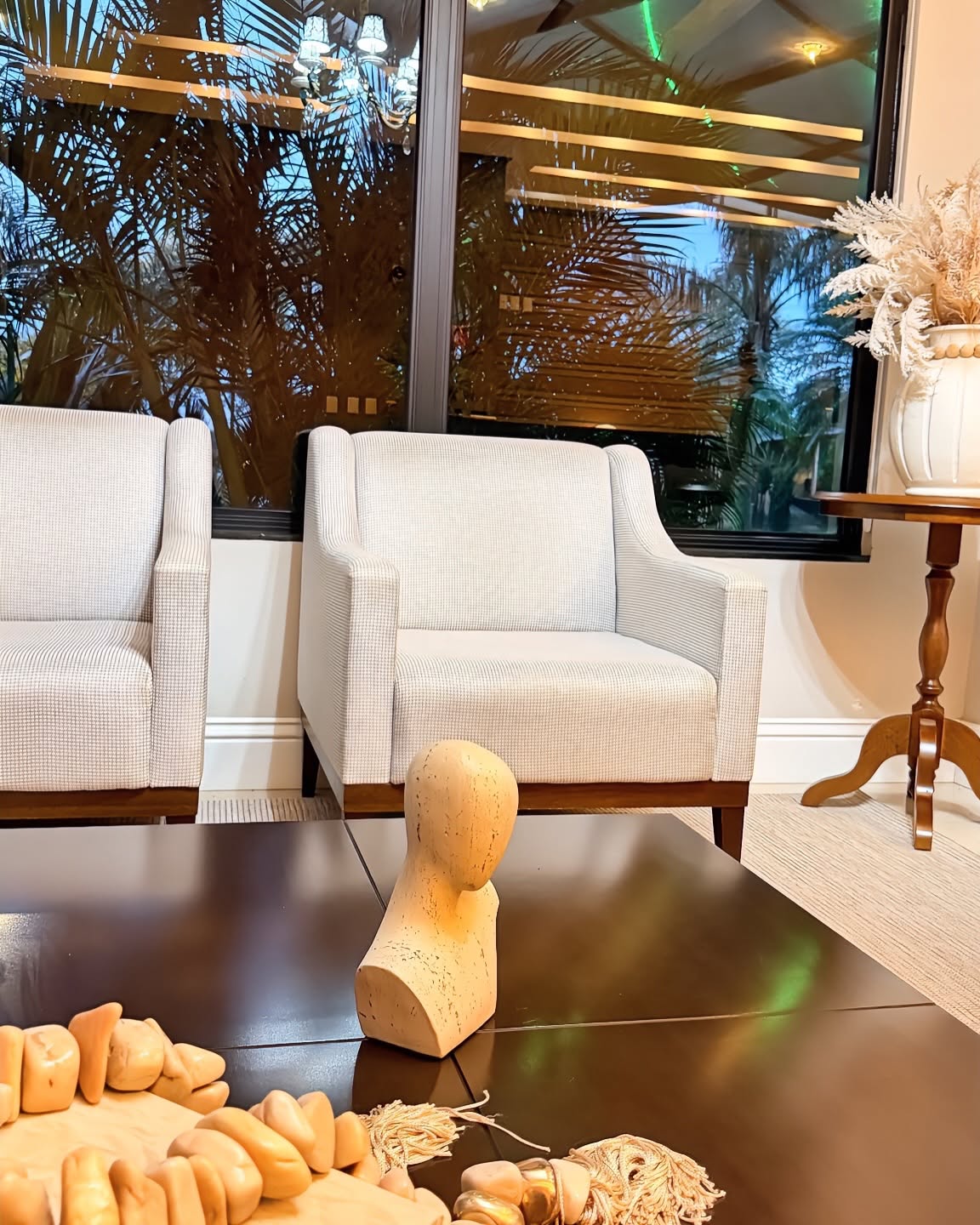 Poltronas claras junto à janela, com objetos de decoração sobre a mesa de centro